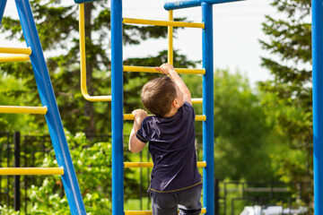 A little caucasian athletic boy climbs on the horizontal bars on the playground. A sporty child does exercises on the monkey bars in kindergarten. Sports and activities. Healthy lifestyle