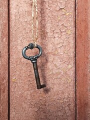 Old retro metal key hanging on twine string on the background of old rustic cracked door. 