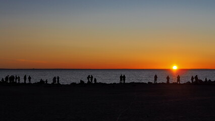 Romantic landscape. Silhouettes of people seeing off the sun on the seashore against the backdrop of a colorful sunset.