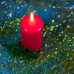 The burning red round candle with the golden tinsel and the little fir branch. Top view. New year, Christmas background