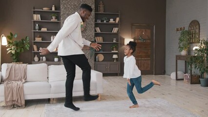 African family dancing in living room celebrate moving day. American biracial father with child girl daughter jumping moves legs dance to music funny home party dad with kid schoolgirl enjoy hobby