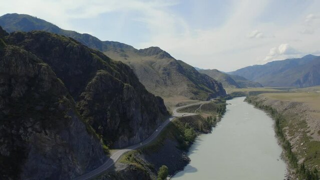 Traffic cars on Chuya highway road between mountains and Katun river under blue sky in Altai, Siberia, Russia. Beautiful summer nature landscape at during daytime. Aerial view from a drone