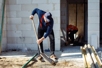 Worker builders, men in coveralls and caps, labors preparing basement floor for building new house,...