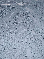 Abstract background. Large drops of rain on the light blue roof of the car.