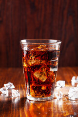 glass of cold cola soft drink with ice on wooden background