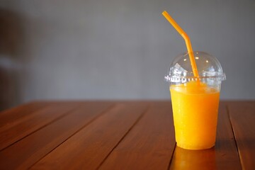 Take away glass of fresh orange juice with orange straw on wooden table in a cafe selective focus
