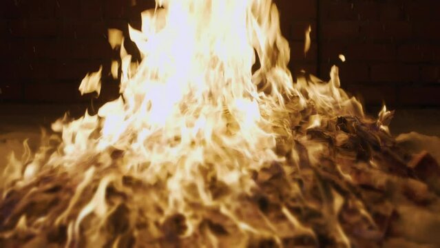 Slow motion, big pile of cash money on the snow burns in backyard near brick wall, strong bright flame, russian rubles banknotes set on fire, dark winter night.