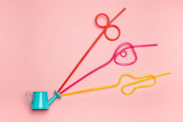 Blue watering can multicoloured drinking straws on a pink background. Minimalistic summer concept.