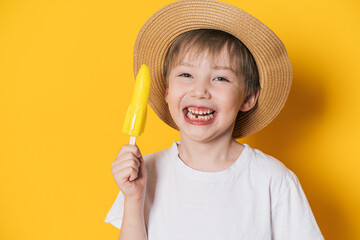 Laughing boy in hat holding rocket-shaped ice cream against yellow background.