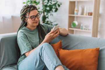 Obraz premium Girl with pigtails on her head holding smartphone while sitting on the couch.