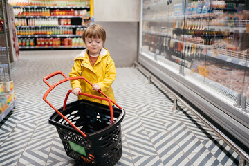 child in the market with a grocery cart, wearing a yellow jacket and jeans