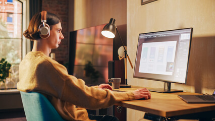 Young Handsome Man Working from Home on Desktop Computer in Sunny Stylish Loft Apartment. Creative Designer Wearing Cozy Yellow Sweater and Headphones. Urban City View from Big Window.