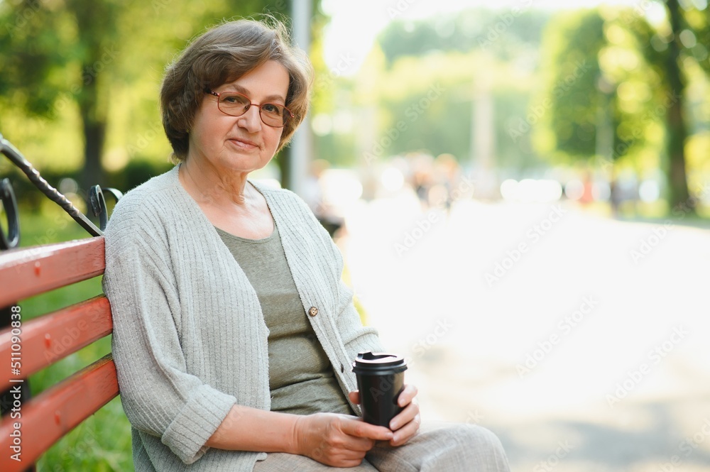 Canvas Prints Elderly woman sitting and relaxing on a bench outdoors in park