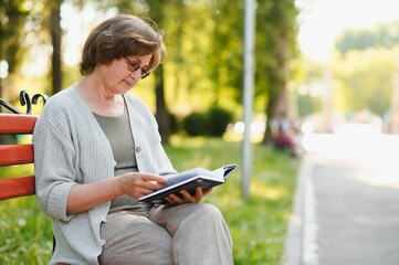 Retired woman reading a book on the bench
