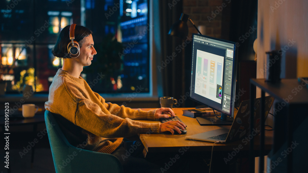 Aufkleber young handsome man working from home on desktop computer in stylish loft apartment in the evening. c
