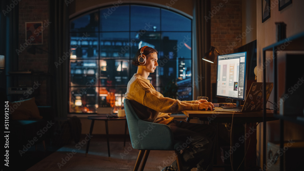 Poster young handsome man working from home on desktop computer in stylish loft apartment in the evening. c