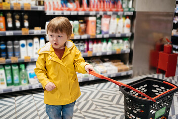 child in the market with a grocery cart, wearing a yellow jacket and jeans