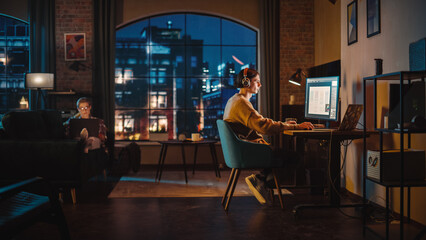 Young Couple Spending Time at Home, Working on Computers from Their Stylish Loft Apartment in the Evening. Female Resting on the Sofa and Browsing Social Media on Laptop. Man Designing UX Interface. - obrazy, fototapety, plakaty