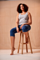 Studio Portrait Shot Of Body Positive Woman Sitting On Stool