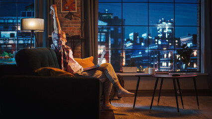 Young Beautiful Woman Sitting on Couch, Using Laptop Computer in Stylish Loft Apartment in the...
