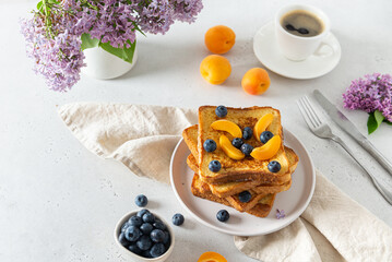 Sweet french toast with berries and syrup served on plate. Copy space for text. Healthy breakfast: toasts with blueberry and apricots and a cup of coffee on white background with lilac flowers