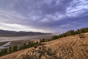 Evening, a view from the mountain to the drying riverbed. The sky is covered with clouds, along the riverbed the wind accelerates the sand suspension.