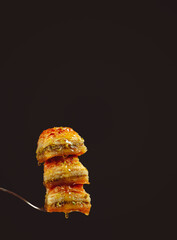 three delicious honey baklavas with pistachios on a fork on a black background, side view, copyspace