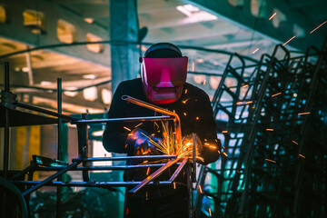 A welder in production is engaged in the manufacture of products. In a mask, in gloves, sparks fly