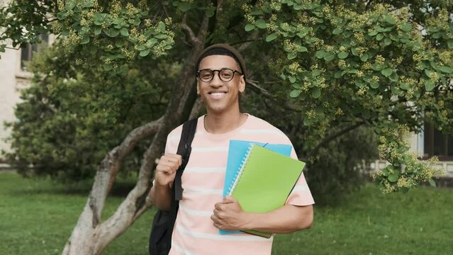 Portrait of smling young African American college student with a backpack and books outdoor with university and campus on the background