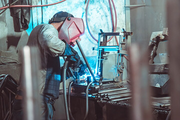  A welder in production is engaged in the manufacture of products. In a mask, in gloves, sparks fly