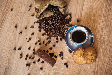 Roasted coffee beans in little bag and cup of coffee with drink on dark wooden surface, nearby lies...