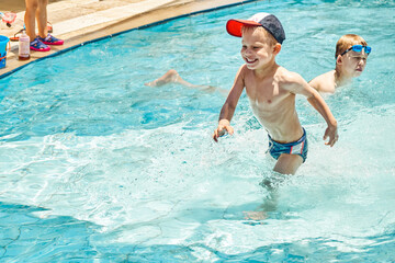 Cute brothers enjoy swimming in children pool at hotel territory. Preschooler in cap and schoolboy in goggles splash in clear water on vacation