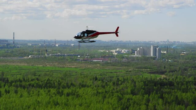 Helicopter blue white red colors flies against a background of blue sky and green fields and buildings on a sunny day. Bell helicopter flies in flight. film grain texture. Pixel texture. Defocus.