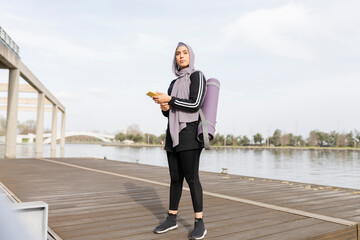 sporty muslim woman mat and smartphone, During her training, a Muslim woman dressed in athletic clothing takes a break in the fresh