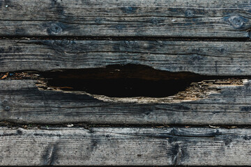 Big crack or hole in a dark black wooden plank
