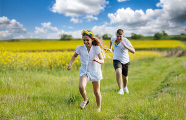 Teenagers: brother and sister are running and enjoying weather, in meadow against cloudy sky