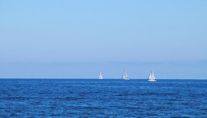 Barcos de vela navegando en el horizonte en la playa de la Malvarrosa en Valencia, España. El mar Mediterráneo con un azul intenso en un claro día de invierno.