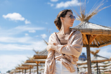 Smiling girl in sunglasses against a stormy sea. A bright sunny day. Straw sun loungers