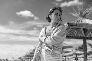 Fototapeta premium Smiling girl in sunglasses against a stormy sea. A bright sunny day. Straw sun loungers