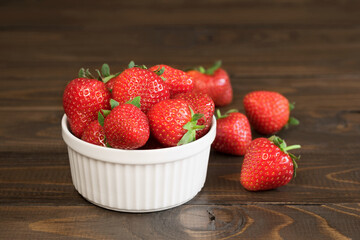 Fresh ripe delicious strawberries in a white bowl on a rustic brown table. Close-up.