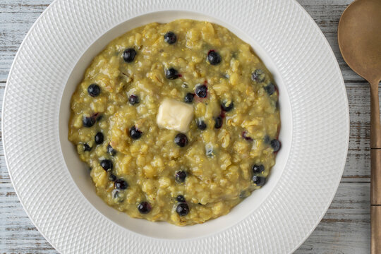 Plain oatmeal porridge with blueberries, butter, turmeric and honey in white plate