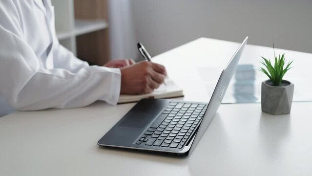 Online diagnostics. Electronic medical data. Digital record. Unrecognizable male doctor in white coat typing prescription using laptop at modern workplace.
