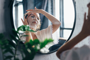 Home skin care. A woman applies a sheet mask to her face