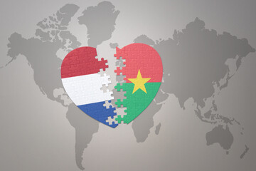puzzle heart with the national flag of burkina faso and netherlands on a world map background.Concept.