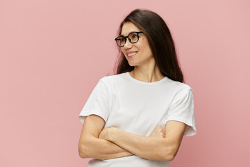Fototapeta premium portrait of a cute, attractive brunette in a white tank top on a pink background, with a pleasant smile, standing in glasses for vision