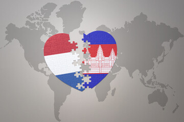 puzzle heart with the national flag of cambodia and netherlands on a world map background.Concept.