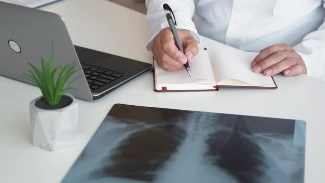 Lung examination. Diagnostic radiology. Medical record. Unrecognizable male doctor working with chest xray scan using laptop taking notes at workplace.