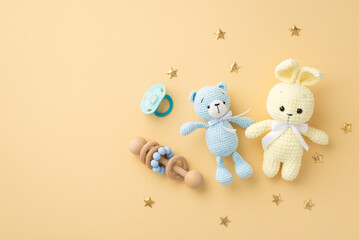 Baby accessories concept. Top view photo of knitted bunny and teddy-bear toys wooden rattle blue pacifier and gold stars on isolated pastel beige background with copyspace