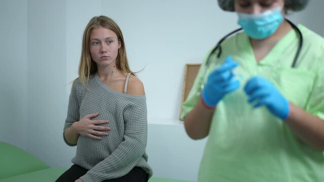 Portrait of young pregnant woman touching belly sitting in vaccination center as doctor filling in syringe with coronavirus vaccine. Caucasian expectant vaccinating on Covid-19 pandemic outbreak