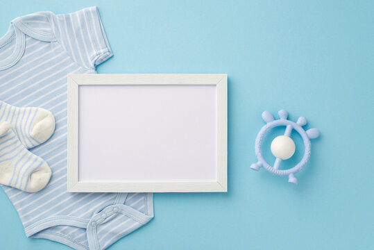 Baby accessories concept. Top view photo of photo frame blue bodysuit socks and rattle toy on isolated pastel blue background with copyspace